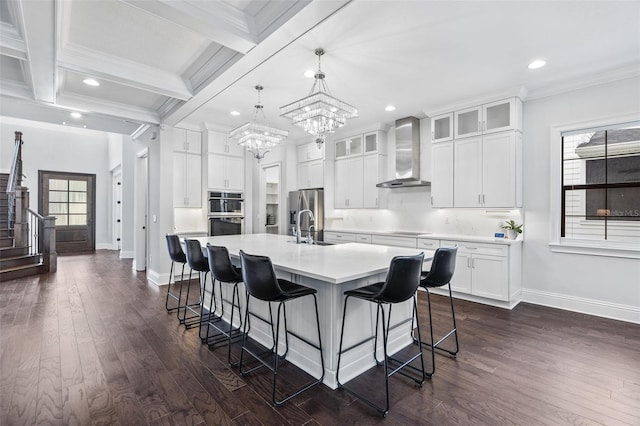 kitchen featuring sink, white cabinetry, hanging light fixtures, a center island with sink, and wall chimney range hood