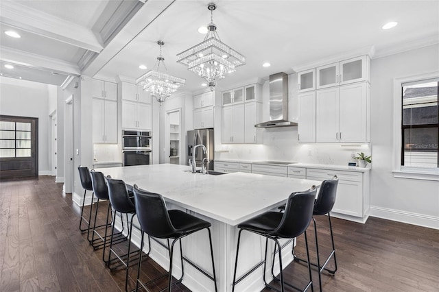 kitchen with pendant lighting, wall chimney range hood, white cabinetry, and a center island with sink