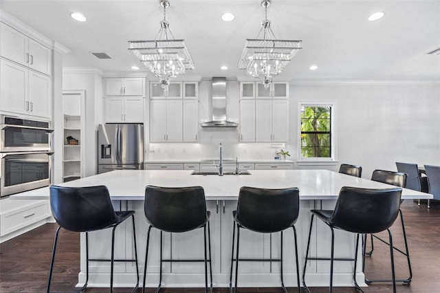 kitchen featuring appliances with stainless steel finishes, a breakfast bar, sink, wall chimney range hood, and a spacious island