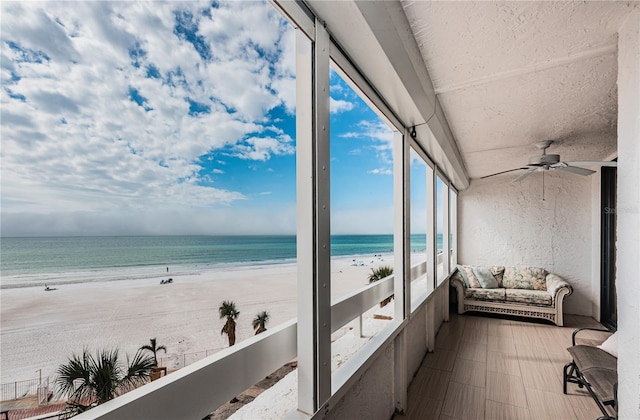 sunroom with a view of the beach, ceiling fan, and a water view