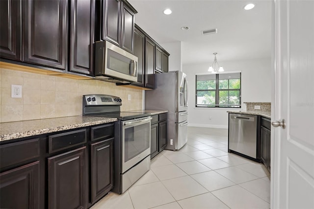 kitchen with light tile patterned floors, appliances with stainless steel finishes, hanging light fixtures, light stone countertops, and decorative backsplash