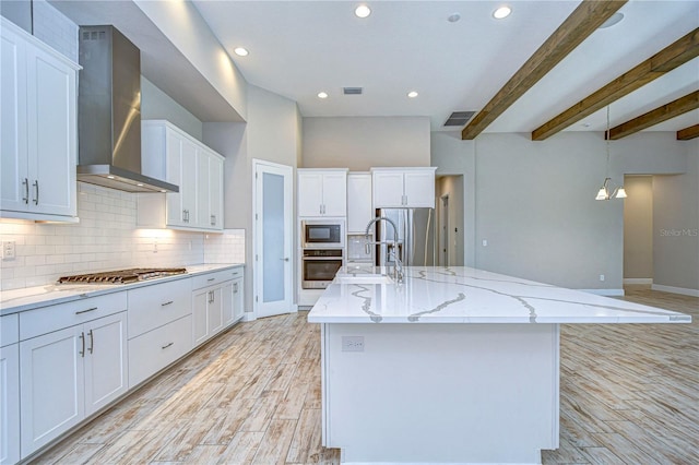 kitchen featuring appliances with stainless steel finishes, white cabinetry, hanging light fixtures, wall chimney exhaust hood, and a large island with sink