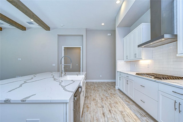 kitchen featuring light stone counters, tasteful backsplash, appliances with stainless steel finishes, wall chimney range hood, and white cabinets