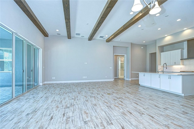 unfurnished living room with beamed ceiling, sink, an inviting chandelier, and light hardwood / wood-style flooring