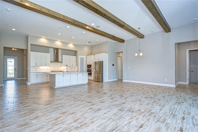 kitchen featuring a kitchen island with sink, white cabinetry, wall chimney exhaust hood, and appliances with stainless steel finishes