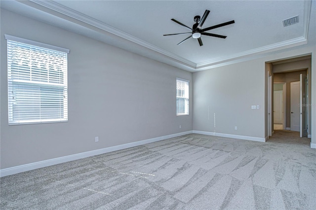 unfurnished room with ceiling fan, light colored carpet, ornamental molding, and a raised ceiling