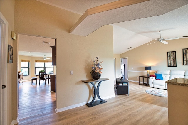 hall with vaulted ceiling, a textured ceiling, and light wood-type flooring