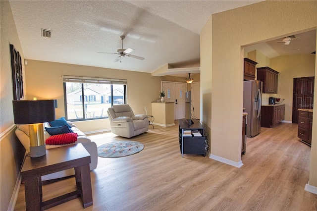 living room with ceiling fan, vaulted ceiling, a textured ceiling, and light wood-type flooring