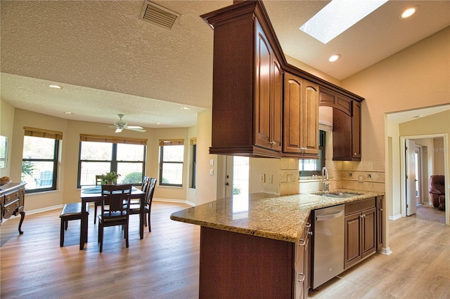 kitchen with sink, stainless steel dishwasher, light stone counters, kitchen peninsula, and light hardwood / wood-style floors