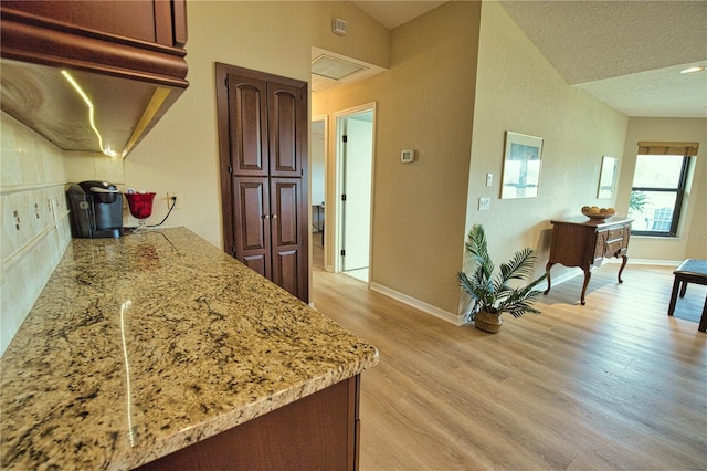 kitchen featuring light stone countertops, vaulted ceiling, light hardwood / wood-style flooring, and a textured ceiling