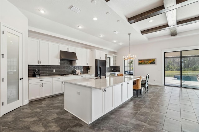 kitchen with beam ceiling, decorative light fixtures, white cabinets, and a center island with sink