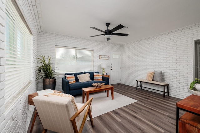 living room with dark wood-type flooring, ceiling fan, and brick wall