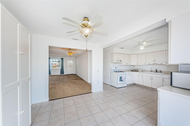 10022 Lily St N Unit N, Pinellas Park, FL 33782 - kitchen featuring white range with gas stovetop, a ceiling fan, white cabinetry, light tile patterned floors, and under cabinet range hood
