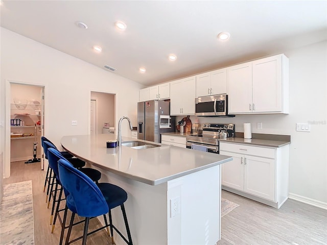 kitchen with a kitchen island with sink, a sink, visible vents, appliances with stainless steel finishes, and a kitchen bar