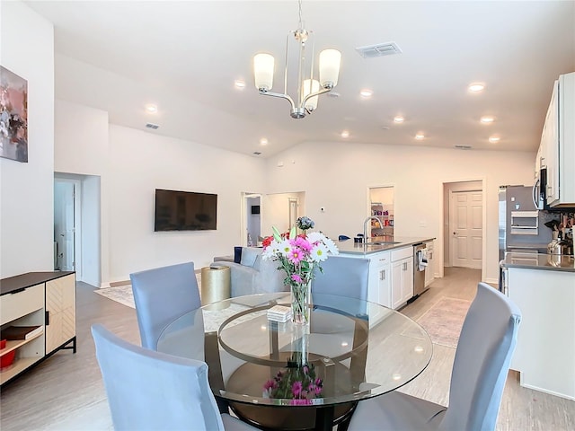 dining area with a chandelier, lofted ceiling, visible vents, and light wood-style floors