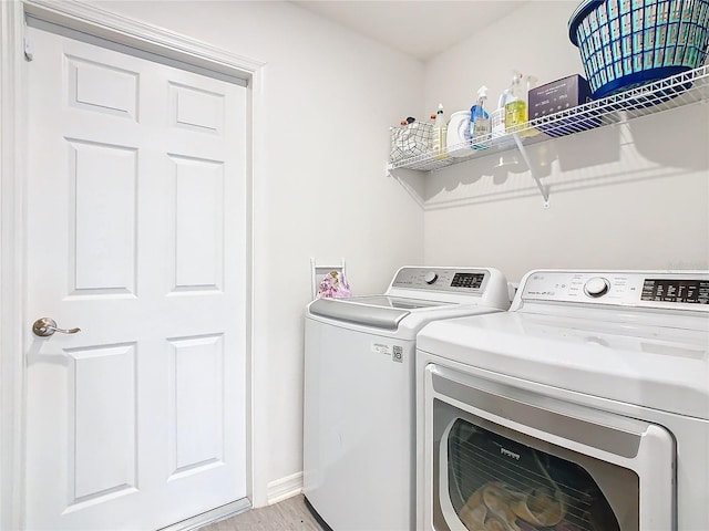 laundry room featuring laundry area, washing machine and clothes dryer, light wood-style flooring, and baseboards