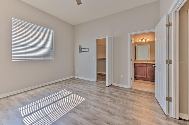 unfurnished bedroom featuring ensuite bath, a walk in closet, a closet, and light wood-type flooring