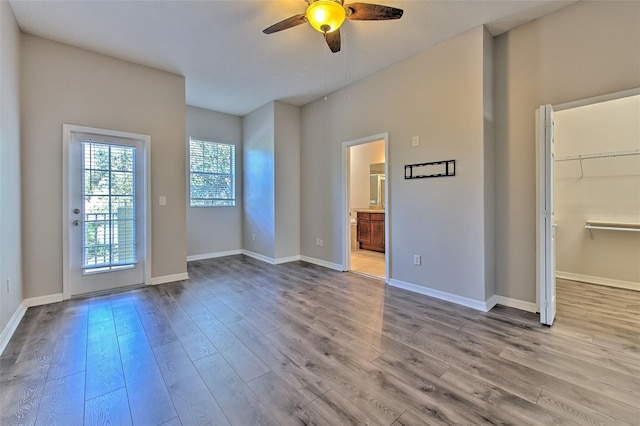 unfurnished bedroom with connected bathroom, a spacious closet, ceiling fan, and light wood-type flooring