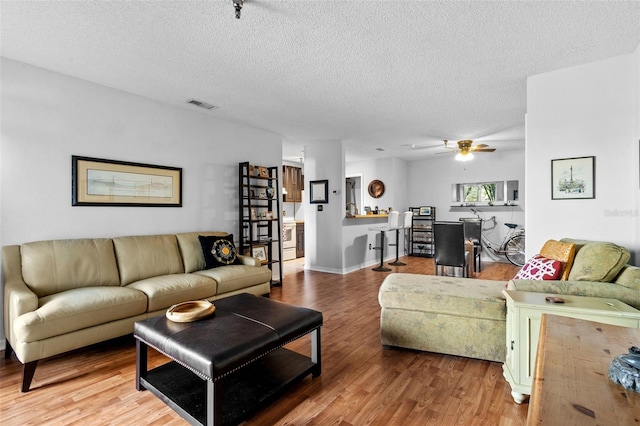 living room featuring wood-type flooring, ceiling fan, and a textured ceiling