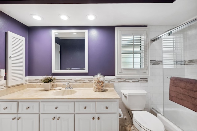 full bathroom with vanity, tile walls, shower / bath combination with glass door, and toilet