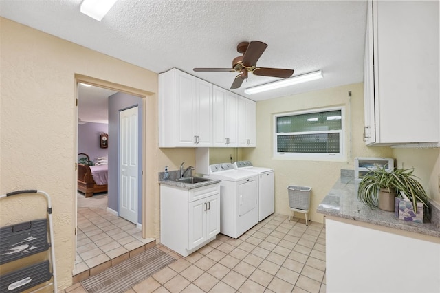 laundry area featuring sink, cabinets, light tile patterned floors, washing machine and clothes dryer, and a textured ceiling