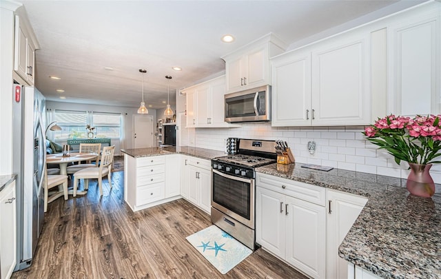 kitchen featuring white cabinetry, hanging light fixtures, appliances with stainless steel finishes, hardwood / wood-style flooring, and decorative backsplash