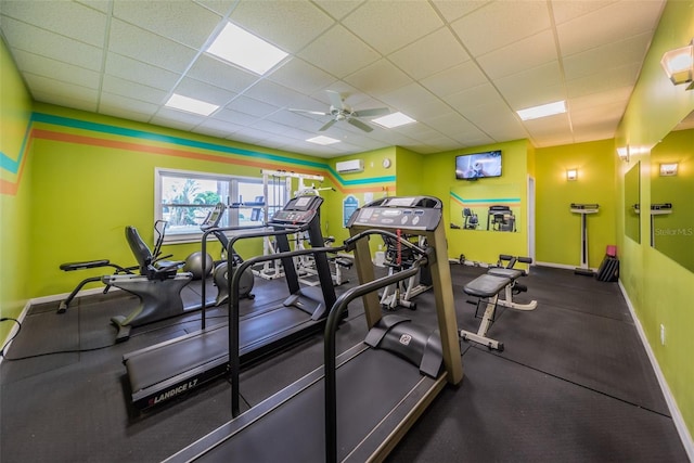 gym with a drop ceiling, an AC wall unit, and ceiling fan