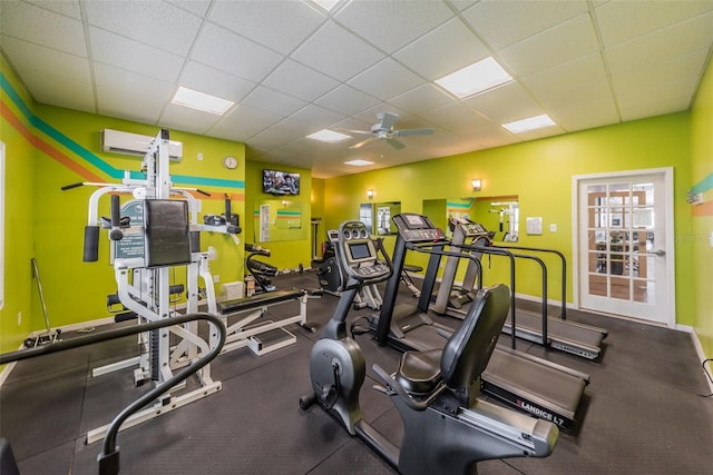 exercise room featuring ceiling fan, an AC wall unit, and a drop ceiling