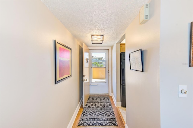 hallway with a textured ceiling and light hardwood / wood-style flooring