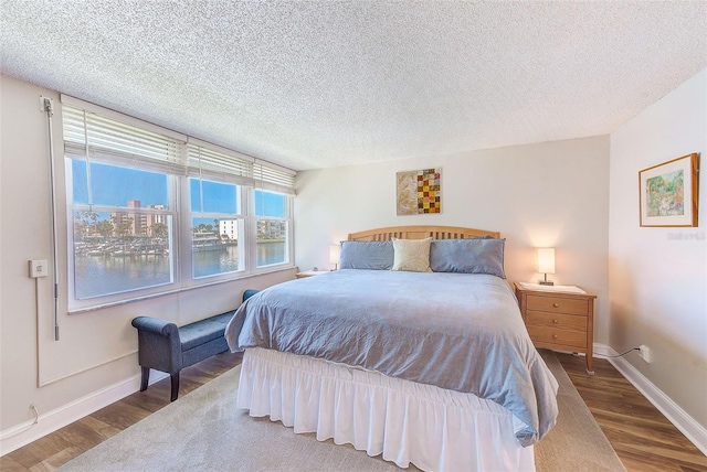 bedroom with dark wood-type flooring, a textured ceiling, and a water view