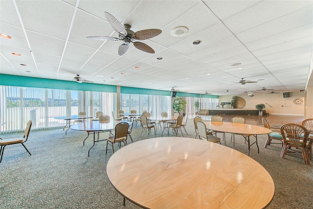 carpeted dining space with a water view, a drop ceiling, and ceiling fan