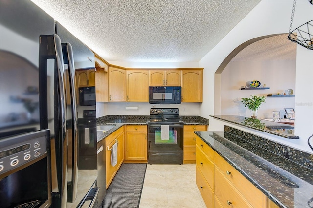 kitchen featuring a textured ceiling, light tile patterned floors, hanging light fixtures, dark stone counters, and black appliances