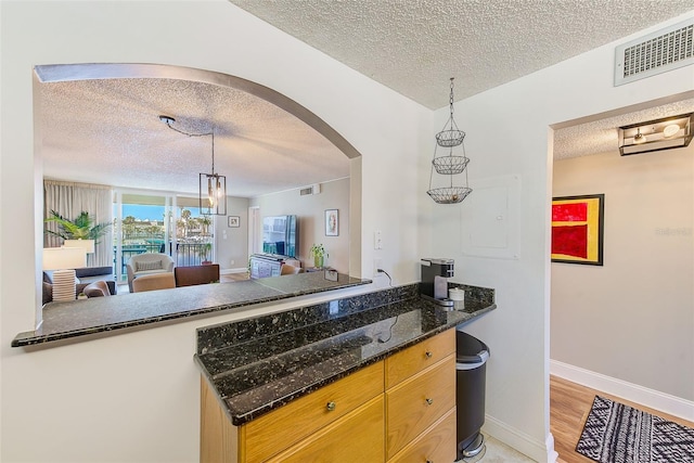 kitchen featuring light hardwood / wood-style floors, dark stone countertops, a textured ceiling, and decorative light fixtures