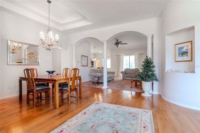 dining area featuring a tray ceiling, light hardwood / wood-style flooring, ceiling fan, and ornate columns