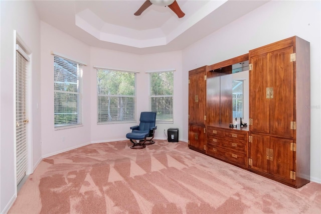 living area featuring a raised ceiling, light carpet, and ceiling fan