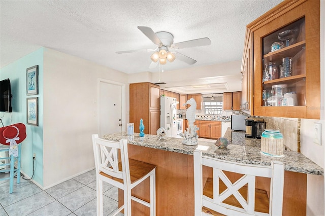 kitchen featuring a kitchen bar, white refrigerator with ice dispenser, light tile patterned floors, light stone counters, and kitchen peninsula