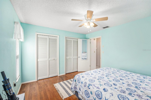 bedroom with ceiling fan, a textured ceiling, wood-type flooring, and multiple closets