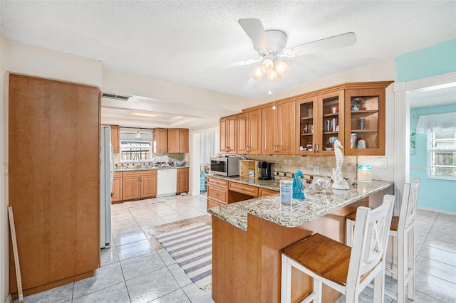 kitchen with sink, white dishwasher, light stone counters, a kitchen bar, and kitchen peninsula