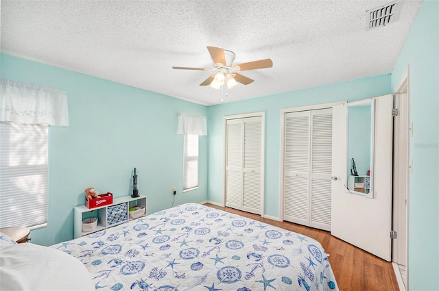 bedroom with ceiling fan, two closets, a textured ceiling, and light hardwood / wood-style flooring