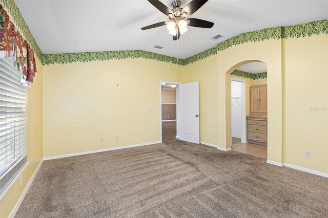 unfurnished bedroom featuring lofted ceiling, a walk in closet, carpet, ceiling fan, and a textured ceiling