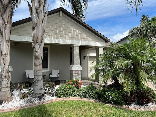 bungalow-style house featuring a porch, stone siding, and stucco siding