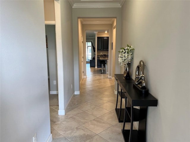 hallway featuring baseboards, light tile patterned floors, and crown molding