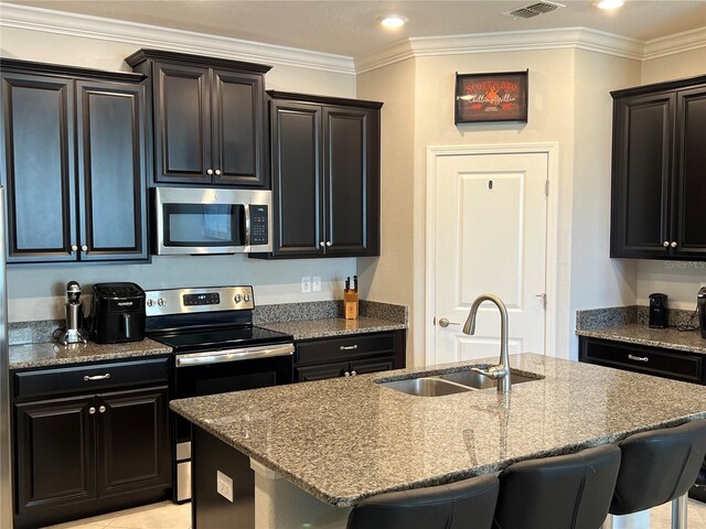 kitchen with a sink, a breakfast bar, a kitchen island with sink, stone counters, and appliances with stainless steel finishes