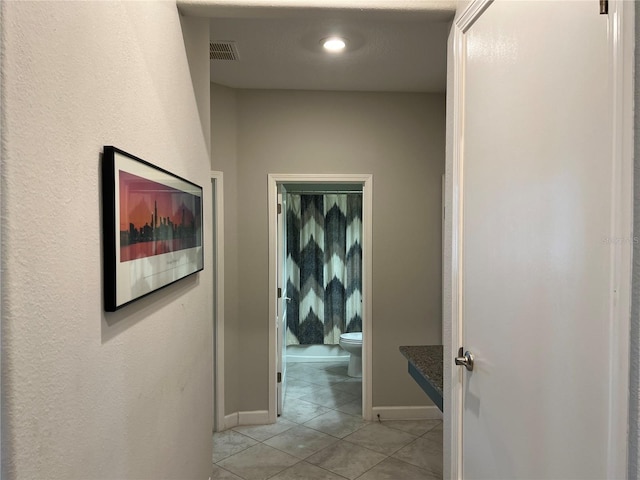 hall with baseboards, visible vents, and light tile patterned floors
