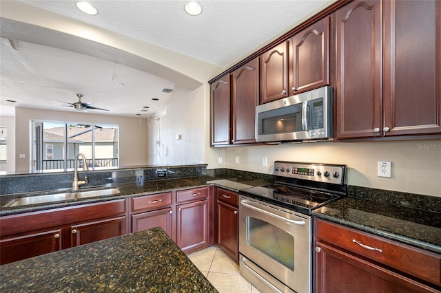 kitchen with sink, dark stone countertops, light tile patterned floors, ceiling fan, and stainless steel appliances