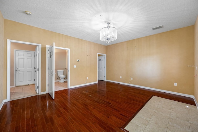 unfurnished bedroom with ensuite bathroom, a chandelier, hardwood / wood-style floors, and a textured ceiling