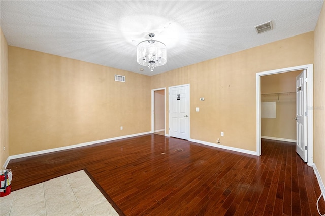 spare room featuring an inviting chandelier, wood-type flooring, and a textured ceiling