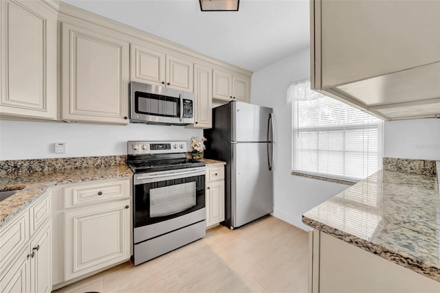 kitchen with appliances with stainless steel finishes, light stone counters, and cream cabinetry