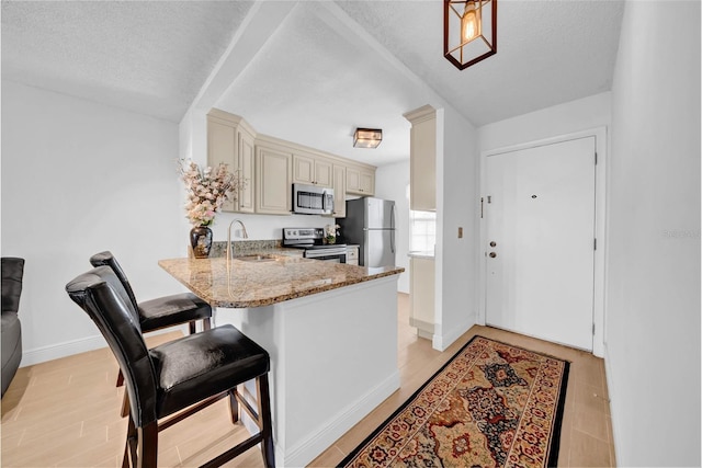 kitchen with sink, stainless steel appliances, light stone countertops, kitchen peninsula, and cream cabinetry