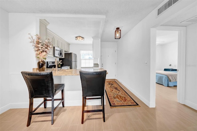 kitchen with light wood-type flooring, appliances with stainless steel finishes, a kitchen breakfast bar, kitchen peninsula, and white cabinets